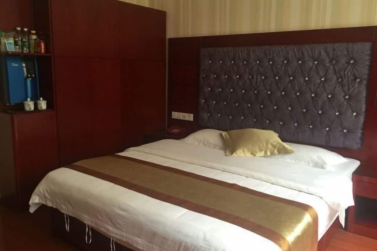 A hotel room with a large bed, a dark tufted headboard, and a wooden wardrobe.
