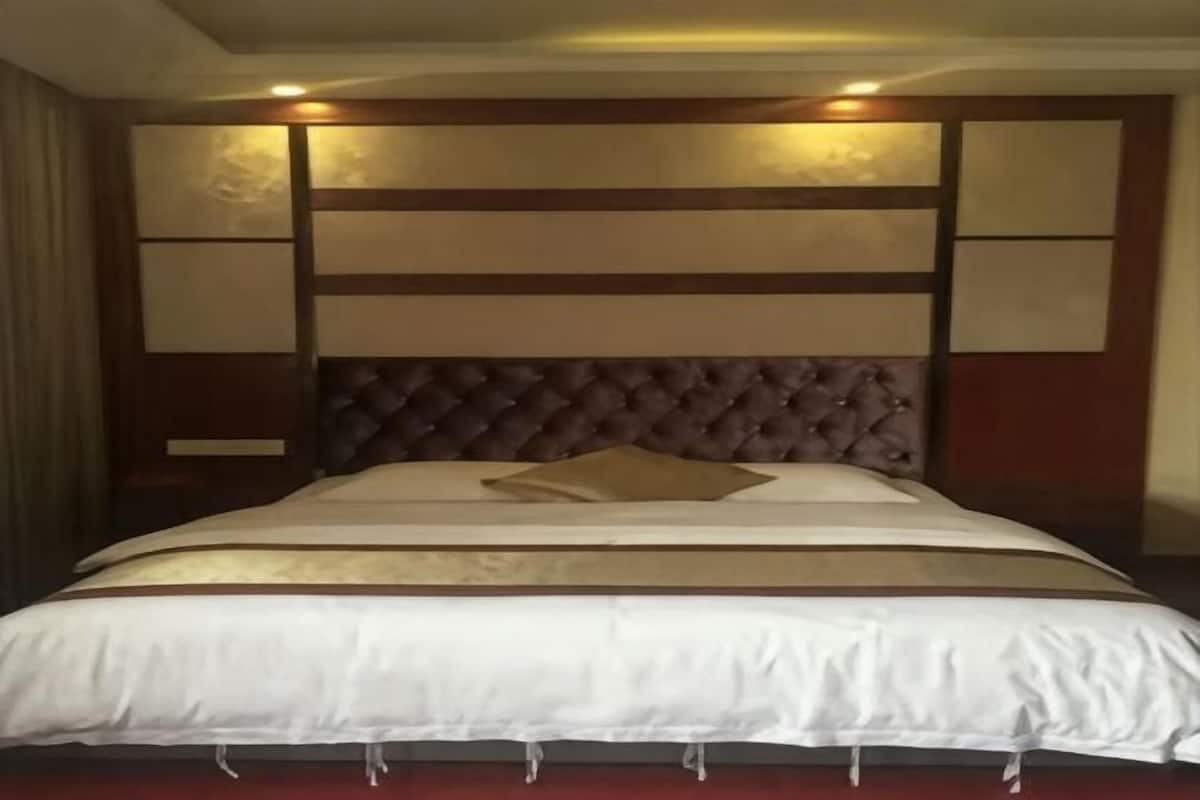 A hotel room with a large bed, a wooden headboard, and a red carpet.