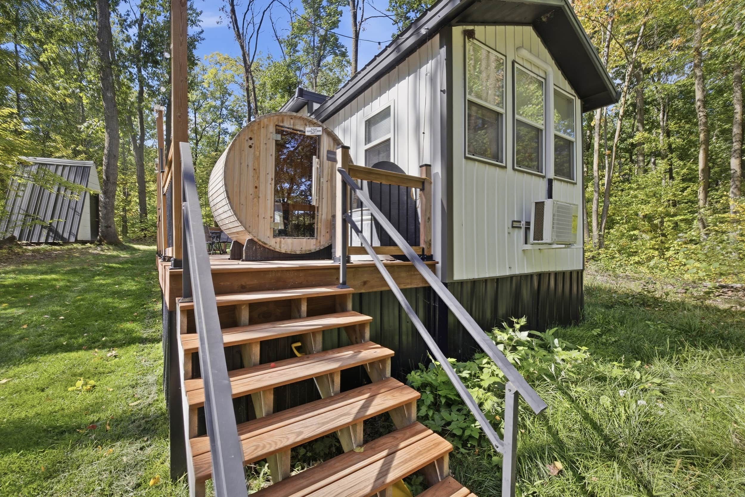 Una pequeña cabaña de madera con una escalera de madera que lleva a una puerta, rodeada de árboles.