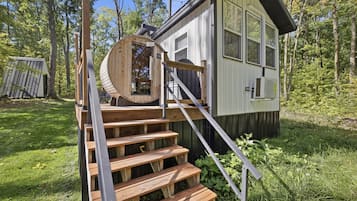Una pequeña cabaña de madera con una escalera de madera que lleva a una puerta, rodeada de árboles.