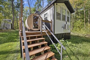 Een klein houten huisje met een houten trap die naar een deur leidt, omgeven door bomen.
