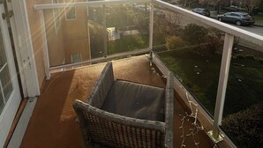 A balcony with a wicker chair, a view of a residential area, and a sunset.