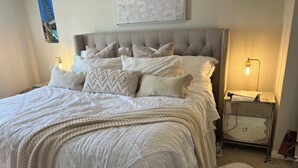 A neatly made bed with a grey upholstered headboard, white bedding, and a decorative pillow.