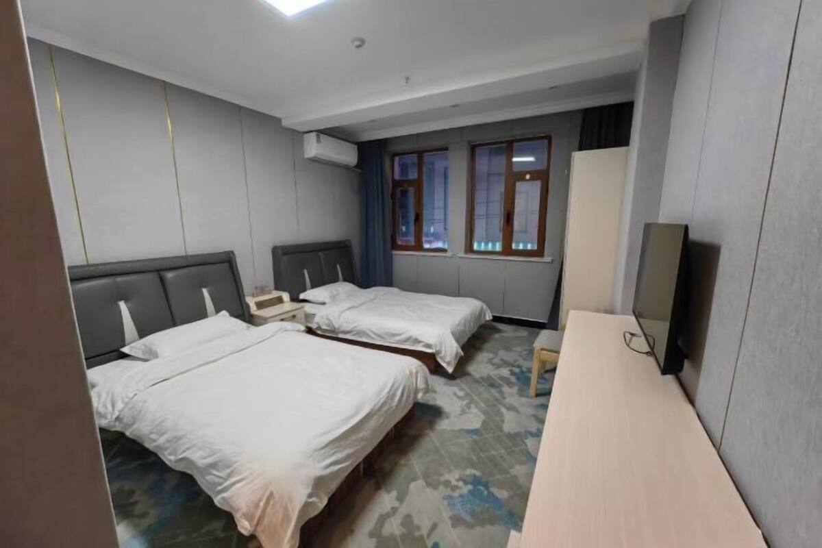 A hotel room with two beds, a desk, a wardrobe, and a window with curtains.
