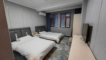 Ein Hotelzimmer mit zwei Betten, einem Schreibtisch, einem Kleiderschrank und einem fensterbepflanzten Fenster.