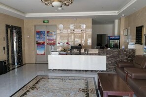 A hotel lobby with a reception desk, a sofa, a coffee table, a patterned rug, and a wall with clocks. - Zihao Hotel (Hunchun Yifen) (Hunchun)