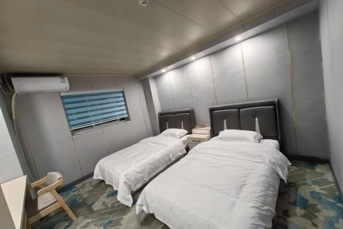 A hotel room with two single beds, a small desk, and a window with blinds.