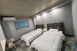 Habitación de hotel con dos camas individuales, un escritorio pequeño y una ventana con persianas.