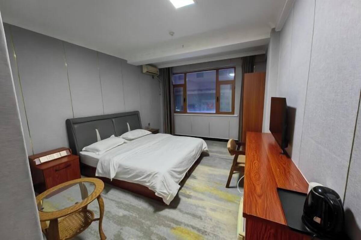 A hotel room with a bed, a desk, a chair, a television, and a window.
