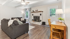 A living room with a fireplace, a sofa, a dining table, and a ceiling fan. - Pet-Friendly Home with Fenced Yard, Monthly stays (Virginia Beach)