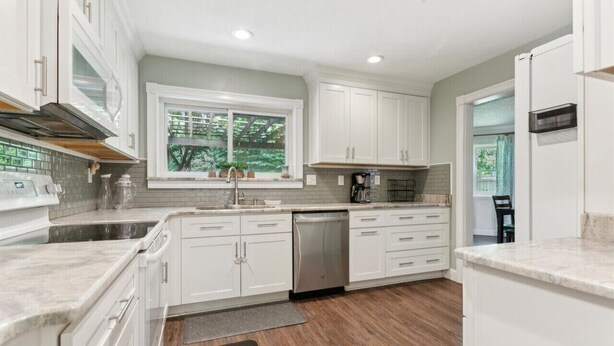 A modern kitchen with white cabinets, a dishwasher, and a window overlooking greenery. - Pet-Friendly Home with Fenced Yard, Monthly stays (Virginia Beach)