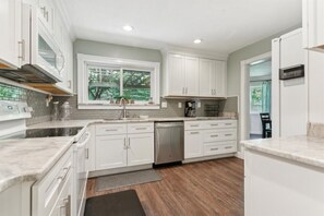 A modern kitchen with white cabinets, a dishwasher, and a window overlooking greenery. - Pet-Friendly Home with Fenced Yard, Monthly stays (Virginia Beach)