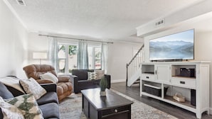 A living room with a dark brown sofa, a black armchair, a coffee table, and a white entertainment unit with a flat-screen TV. - Pet-Friendly Home with Fenced Yard, Monthly stays (Virginia Beach)