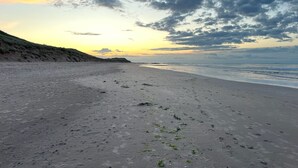 En strand med sandet bredde og en græsklædt dune i baggrunden.