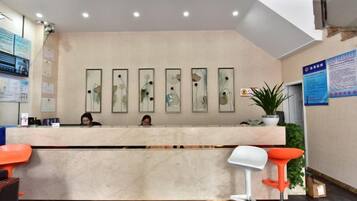 Zona de recepción con mostrador de mármol, dos taburetes naranjas y obras de arte enmarcadas en la pared.