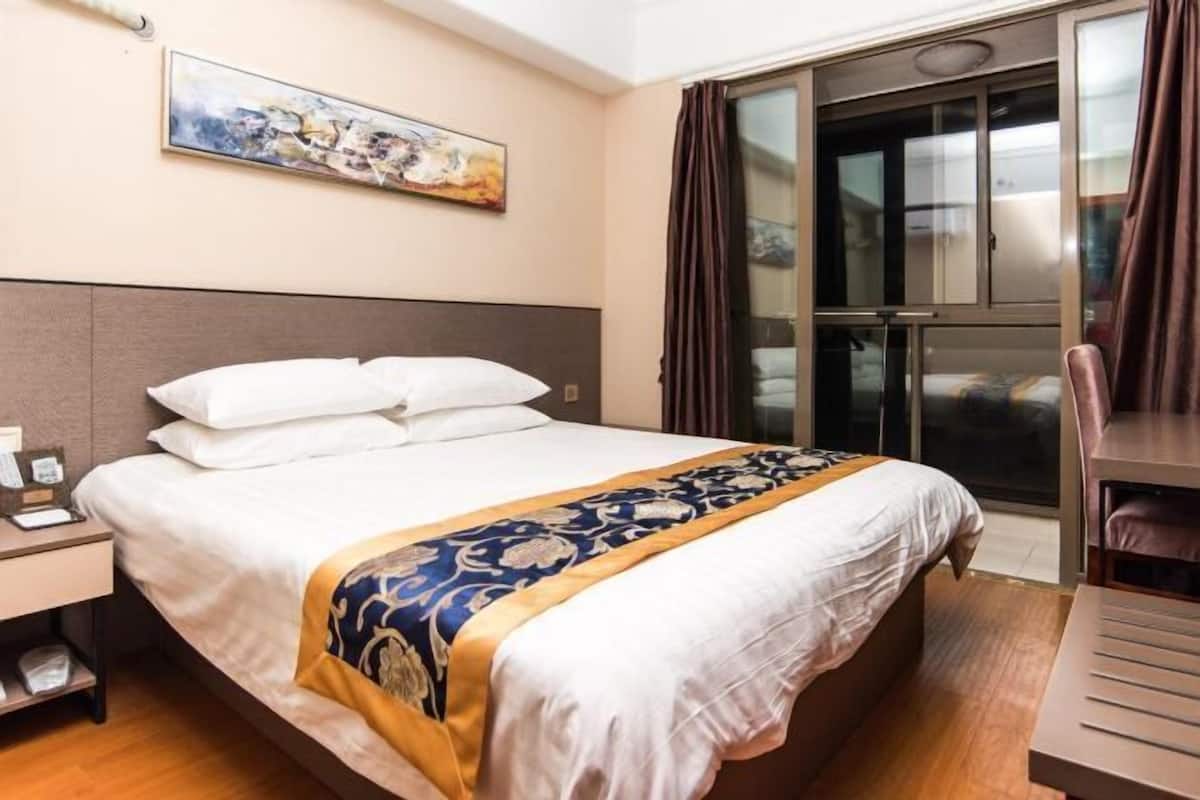 Une chambre d’hôtel comprenant un lit, une table de chevet, un bureau et une porte-fenêtre coulissante donnant sur le balcon.
