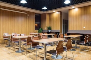Uma área de refeições moderna com paredes de painel de madeira, mesas com estrutura de metal e cadeiras estofadas.