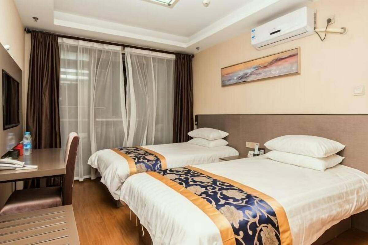 Une chambre d’hôtel avec deux lits, un bureau, une chaise, un appareil de climatisation et un tableau au mur.