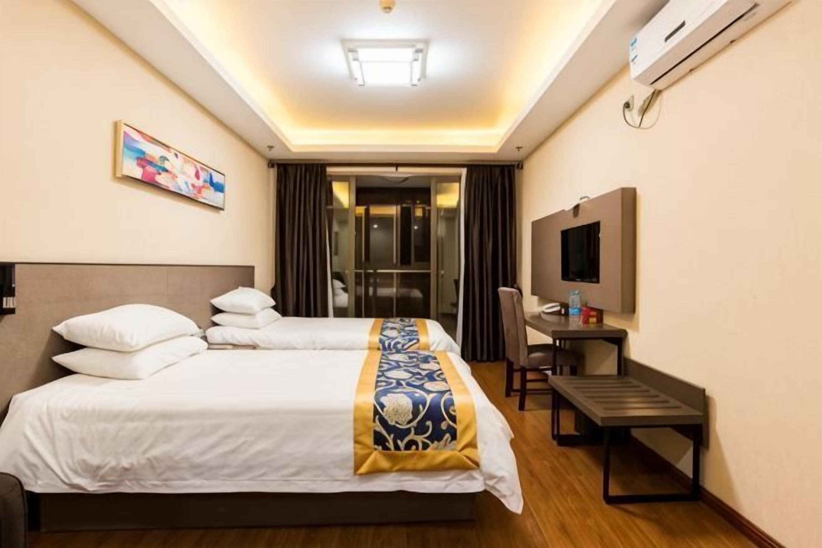 A hotel room with a large bed, a desk, a chair, a television, and an air conditioning unit.