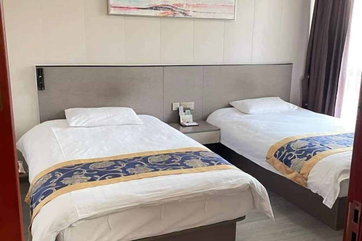 Une chambre d’hôtel avec deux lits, une tête de lit, une table de chevet, un téléphone et un tableau au mur.