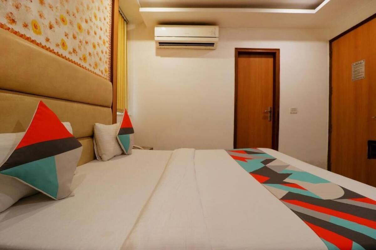 A hotel room with a bed, a wooden door, an air conditioning unit, and a patterned wall.