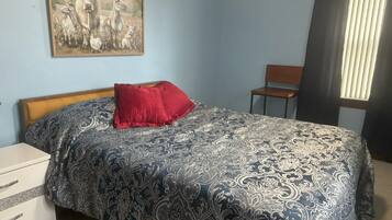 A bedroom with a bed, a nightstand, a chair, and a window with blinds.