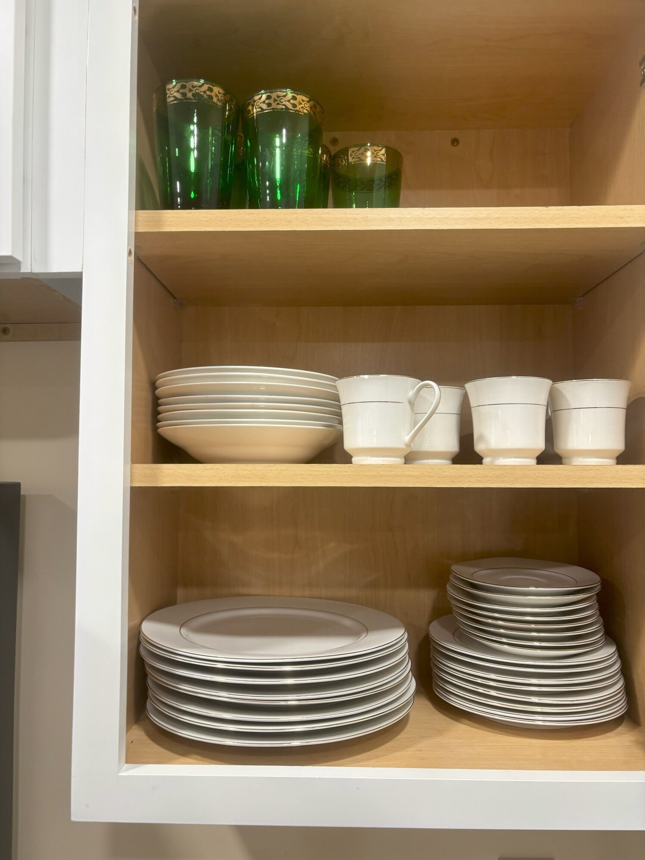 A kitchen cabinet with shelves holding plates, bowls, cups, and decorative glassware.