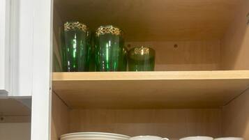 A kitchen cabinet with shelves holding plates, bowls, cups, and decorative glassware.