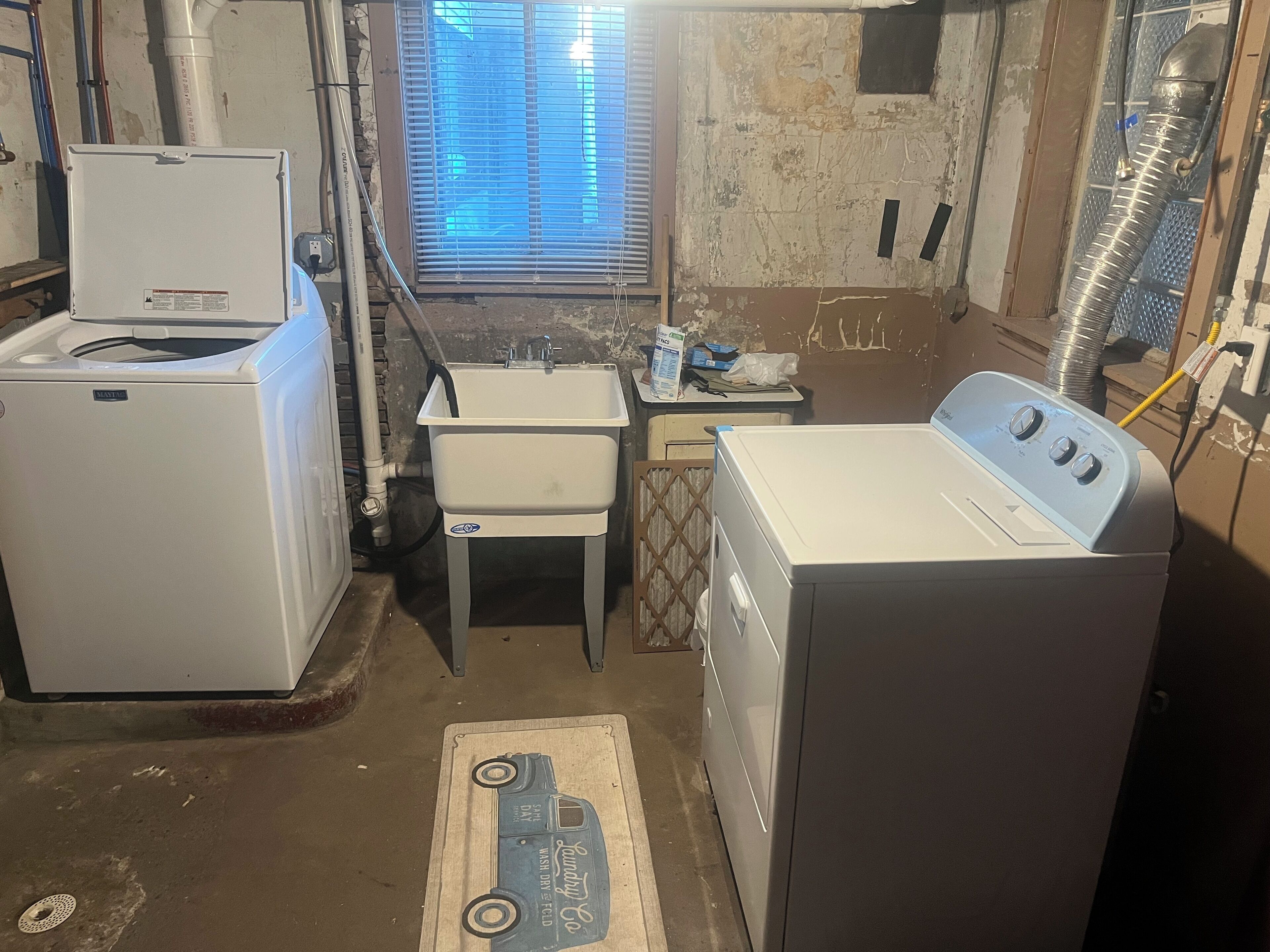 A laundry room with a washing machine, a dryer, a sink, and a window with blinds.