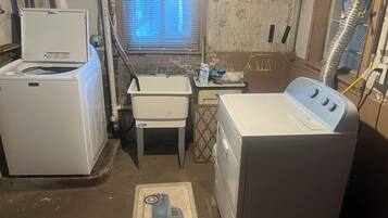A laundry room with a washing machine, a dryer, a sink, and a window with blinds.