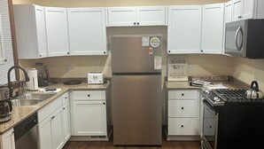 Una cocina con armarios blancos, un refrigerador de acero inoxidable, una estufa y un microondas.