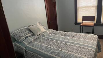 Une chambre à coucher avec un lit, une chaise, une porte et une fenêtre avec des stores.