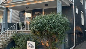 Una casa de dos plantas con un porche y un árbol pequeño en el frente, con un letrero que dice "Ashlin House".