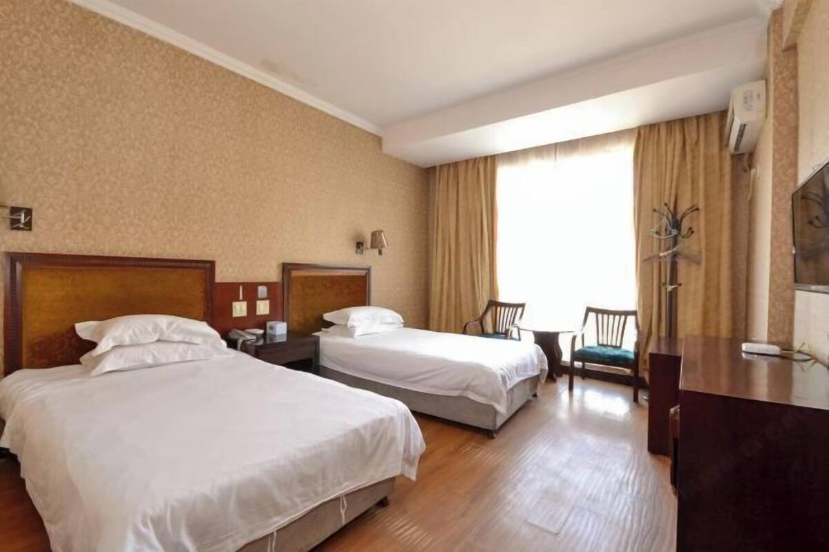 A hotel room with two beds, a desk, a chair, and a large window with curtains.