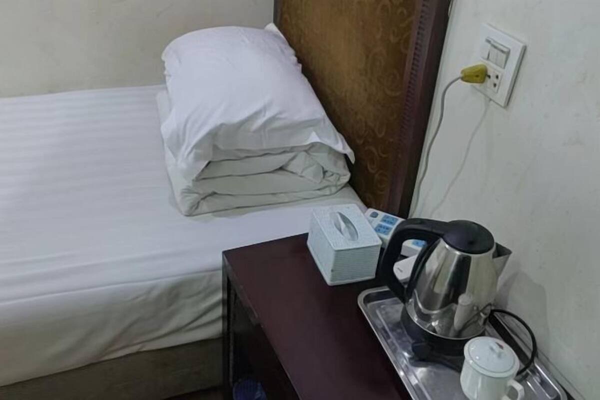 A hotel room with a bed, a bedside table with a tissue box, a kettle, and a cup.