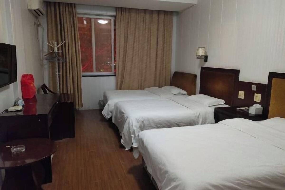 A hotel room with two single beds, a desk with a chair, a TV, and a window with curtains.