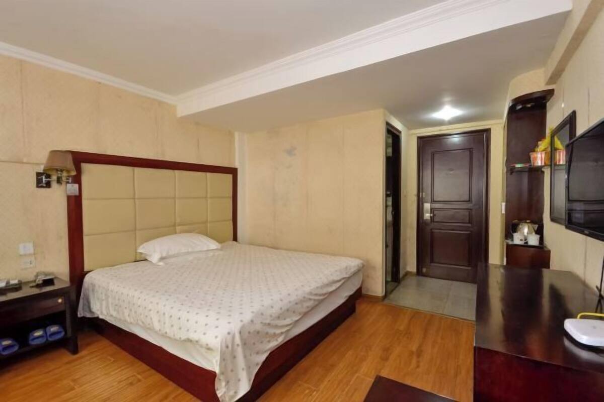 A hotel room with a bed, bedside table, lamp, and a television.