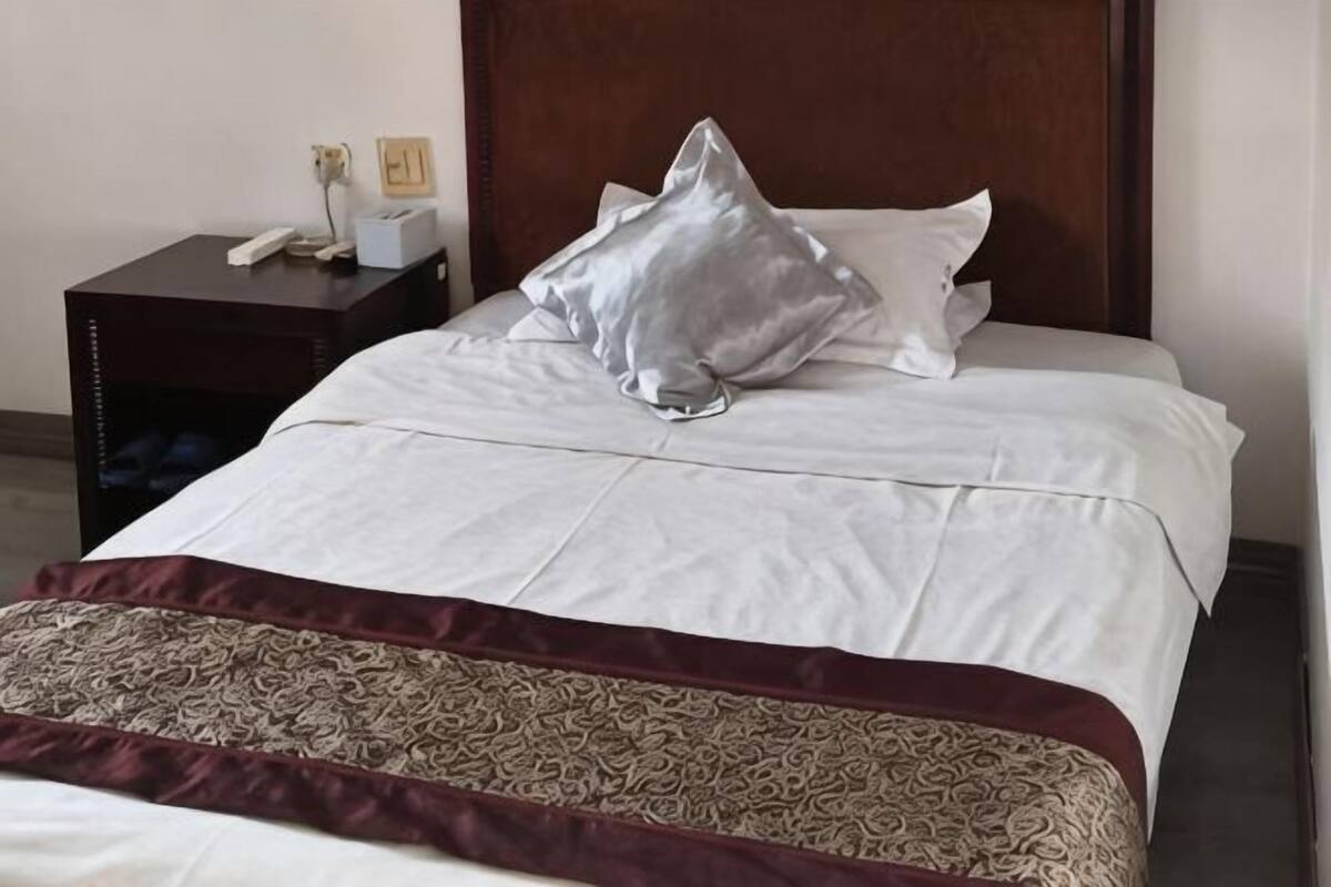 A neatly made bed with a patterned throw, a wooden headboard, and a nightstand with a phone and a lamp.