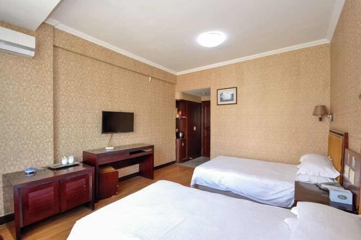 A hotel room with two beds, a desk, a television, and a door leading to another room.