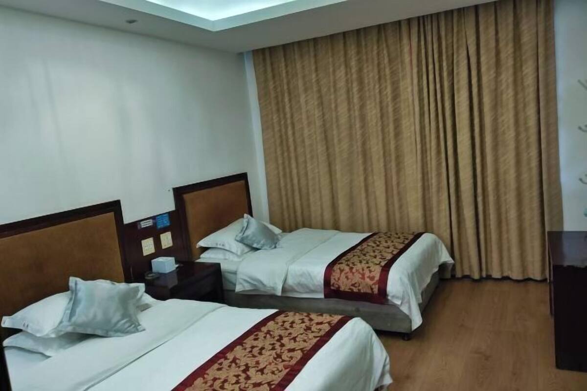 A hotel room with two beds, a wooden headboard, a nightstand, and a large window with curtains.
