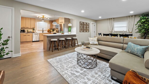 A modern living room with a sofa, coffee table, and a dining area with stools.