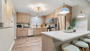 A modern kitchen with wooden cabinets, stainless steel appliances, and a central island with stools. - Chic Oasis/Game Room/Near Base/5 Bedroom (Waukegan)