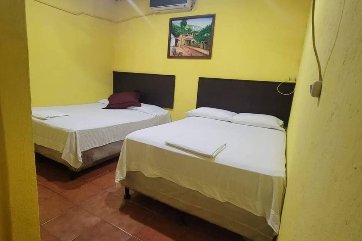A room with two beds, a ceiling fan, an air conditioning unit, and a wall-mounted picture.