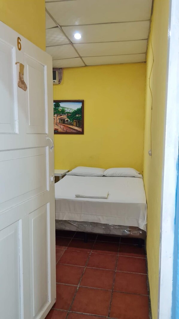 A small, single-room accommodation with a bed, a white wardrobe, and a yellow wall.
