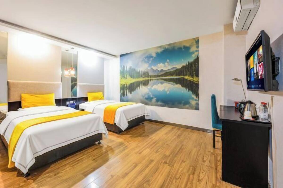 Habitación de hotel con dos camas, un escritorio, un televisor y un cuadro grande de un lago.