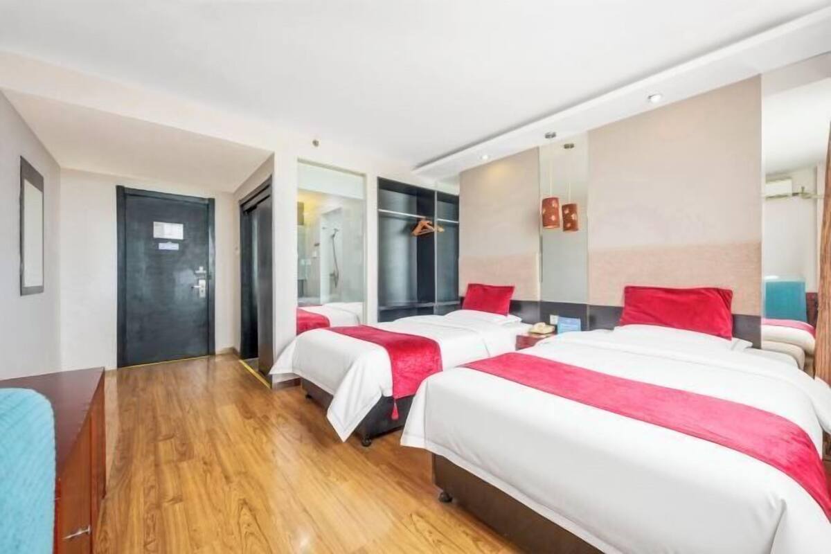 Habitación de hotel con dos camas, suelo de madera, un espejo y una puerta.