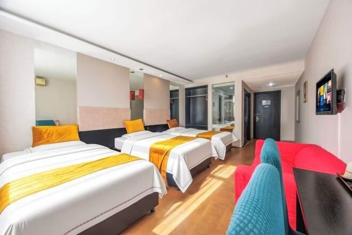 Una habitación de hotel con tres camas, un sofá rojo y un ventanal grande.