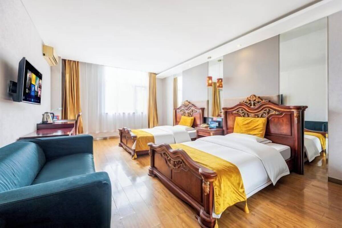 Una habitación de hotel con dos camas, un sofá, un televisor y un espejo grande.