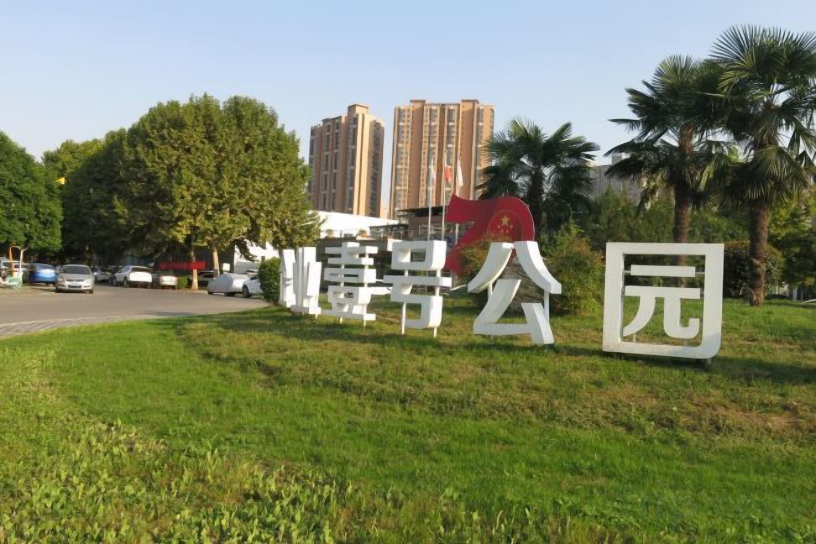 Placa com caracteres chineses, área gramada e palmeiras.