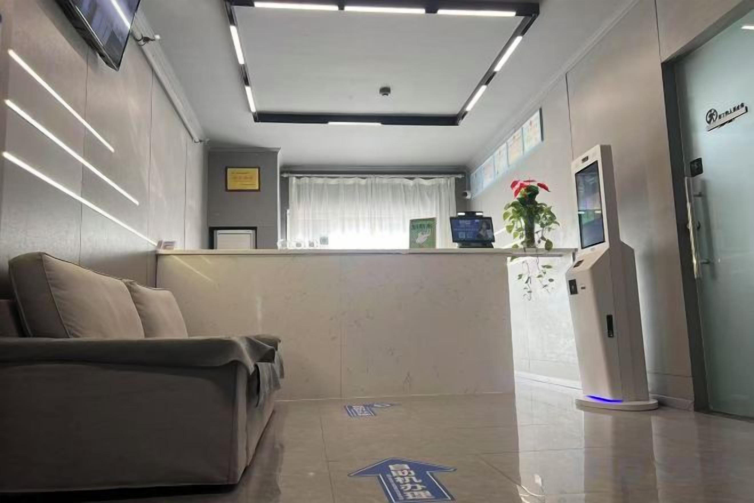 A reception area with a sofa, a reception desk, a plant, and a door with a sign.